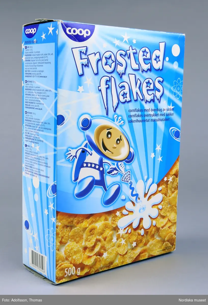 Rektangulär flingförpackning av kartong med heltäckande färgillustrationer. Framsidan upptas av en rymdfigur och texten "Frosted flakes cornflakes med överdrag av socker 500g". Baksidan utgörs av ritpyssel där streck kan dras mellan ett trettital punkter för att en figur ska framträda, enligt instruktion: "Dra ett sträck mellan siffrorna och se vem jag är". På förpackningens kortsidor finns produktinformation. Se länkad fil.