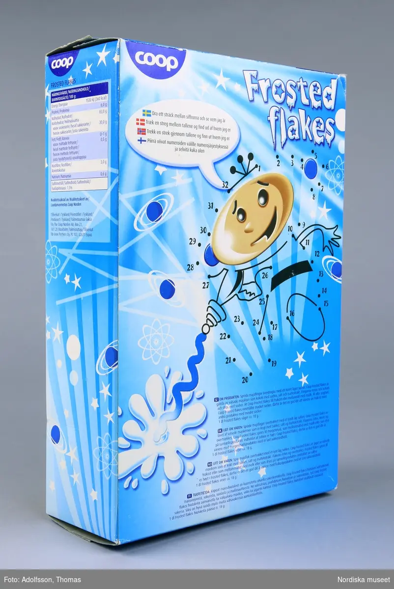 Rektangulär flingförpackning av kartong med heltäckande färgillustrationer. Framsidan upptas av en rymdfigur och texten "Frosted flakes cornflakes med överdrag av socker 500g". Baksidan utgörs av ritpyssel där streck kan dras mellan ett trettital punkter för att en figur ska framträda, enligt instruktion: "Dra ett sträck mellan siffrorna och se vem jag är". På förpackningens kortsidor finns produktinformation. Se länkad fil.