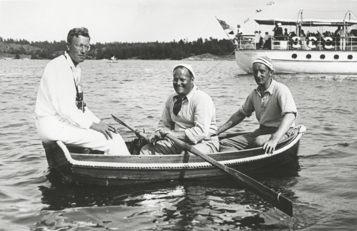 Tre män i en båt under KSSS:s långfärdssegling genom Södermanlands och Östergötlands skärgårdar i juli 1932. I mitten Gunnar Rooth, i aktern David Öhman, i fören oidentifierad person, i bakgrunden Erik Åkerlunds motoryacht STELLA MARINA.