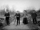 FYRA PERSONER PÅ PROMENAD. 
TVÅ AV DEM LEDER CYKLAR.  
KVINNAN HETER ELSA FRANSSON, FÖDD LINDQVIST.