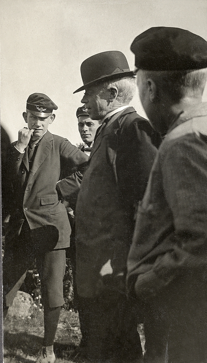 En äldre man i hatt och rock tillsammans med några tonårspojkar i skolmössa m.m.
Under fotot text: " - Ludde - en Hedersman - ".

"Ludde" - lektor Ludvig Larsson (1860-1933) (?).