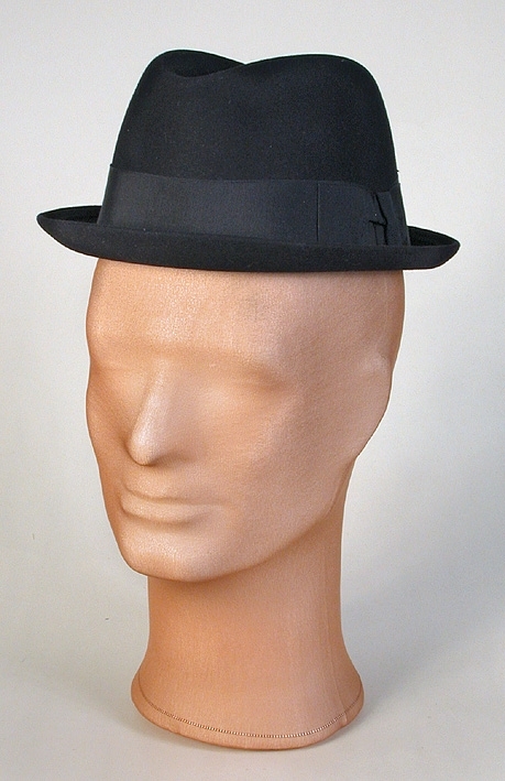 Herrhatt av blå filt. Låg kulle, kraftigt stukad upptill. Smalt brätte, uppvikt bak. 
Mått: Runt kullen 530 mm. Kullens höjd 115 mm. 
Storlek: 55.