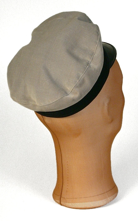 Skärmmössa av grå sammet. Platt kulle, skärm av lack. Kokard av gult och blått mitt fram.
   Mått: Runt kullen 600 mm. Höjd 70 mm. 
   Storlek: 55.