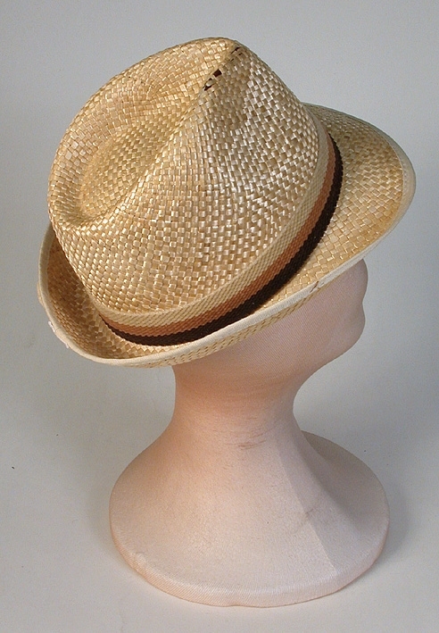 Herrhatt av halm. Tillverkad i Spanien. Ripskantat brätte, uppvikt bak. 
   Mått: Kullens höjd 100 mm. Runt kullen 570 mm. 
   Storlek: 56.