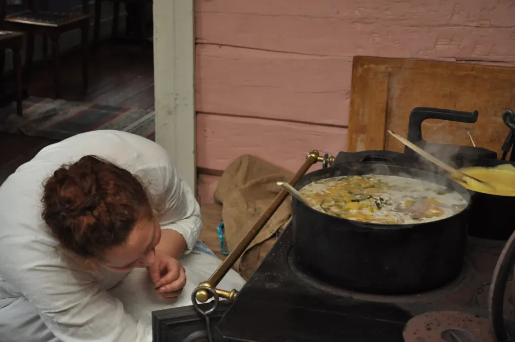 Maren Sofie Løfsgård koker mat på vedkomfyren i Gjersøyen. Rosa vegg på kjøkkenet.