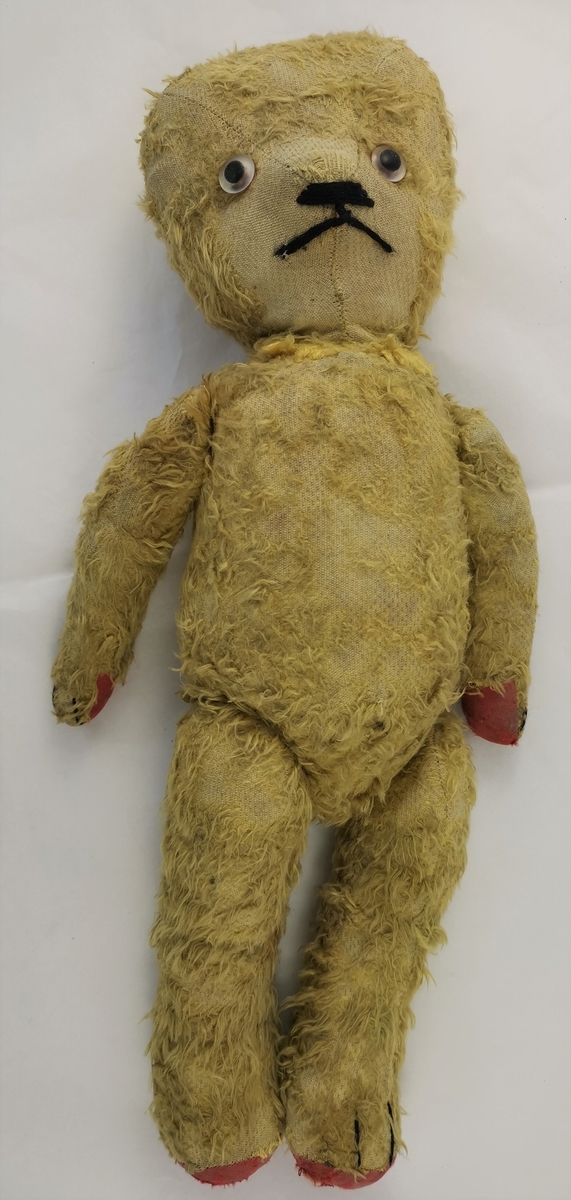 Form: "Teddy-fasong" av eldre, slank type.
Glasaugo, brodert munn og mustasje og markering for poter, Hovudet avspissa mot snute. Kan tr. vera eit Steiff-produkt frå Tyskland.