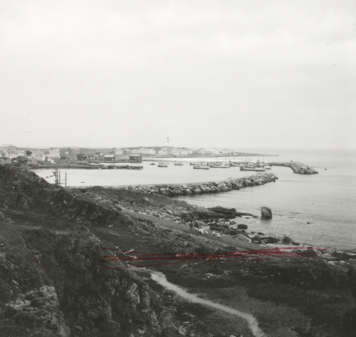 Prospektfotografi med oversikt over havna og bebyggelsen med fyrtårnet på Alnes, Godøy.