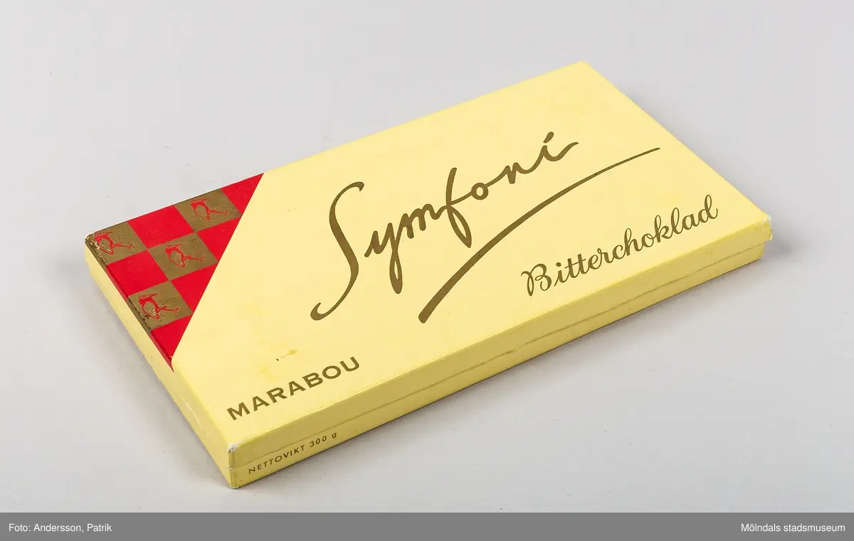 Chokladasken: Symfoni Bitterchoklad 300 g, tillverkad av Marabou troligtvis någon gång under 1950 till 60-talet.

När chokladsken var ny, innehöll den tunna platta fyrkantiga chokladbitar som var cirka 3,5x5cm med inristade mönster snyggt placerade i rader. Asken hade 2 våningar med silkepapper över chokladen fäst på ena långsidan.

Asken är av papp. Den är gul och har röda och guldfärgade detaljer. Texten: "MARABOU Symfoni Bitterchoklad", finns tryckt på locket tillsammans med Marbou-storken. På insidan av locket finns även ett guldfärgat tryck med texten: "AKTIEBOLAGET MARABOU - STOCKHOLM   Marabou"
På lockets ena långsida finns även texten: "NETTOVIKT 300 g", i guldfärgat tryck.