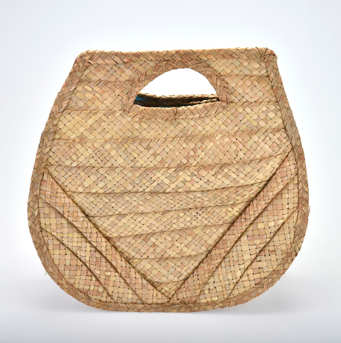 En veske av bast og plast som er flettet og maskinsydd. Basten er flettet. I front (på begge sider) er det 10 vannrette striper som er omtrent 4cm brede. Stripene blir kortere fra øverst og ned mot bunnen (den nederste stripen er kun en liten trekant). På hver side er det 3 skråstilte striper som er flettet med mer "volum". Det er trekantformede håndtak øverst på begge sider. Sidene og bunnen på vesken består av 4 flettede striper. Vesken er foret med plast. Den er blå- og hvitrutet med bilder av diverse frukt og en primus på rutete duk. Mønsteret er repeterende.