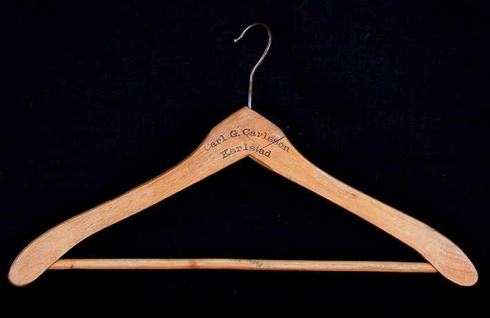 Trägalge med rundade, något bredare ändar. En slå av rundstav i nederkant. Metallkrok i överkant. Svart tryck "Carl G. Carlsson Karlstad" på båda sidor. Carl G. Carlsson Karlstad är mer känt som CGC.