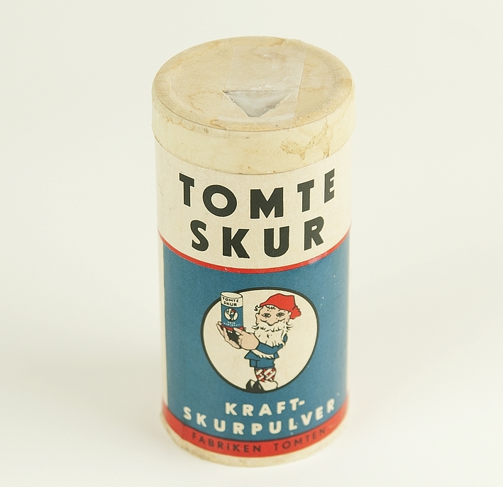 Burk i papp med tomtens löddrande kraftskurpulver. Tryckt logga föreställande glad tomte som håller upp en produkt. Text som förklarar produktens fördelar.