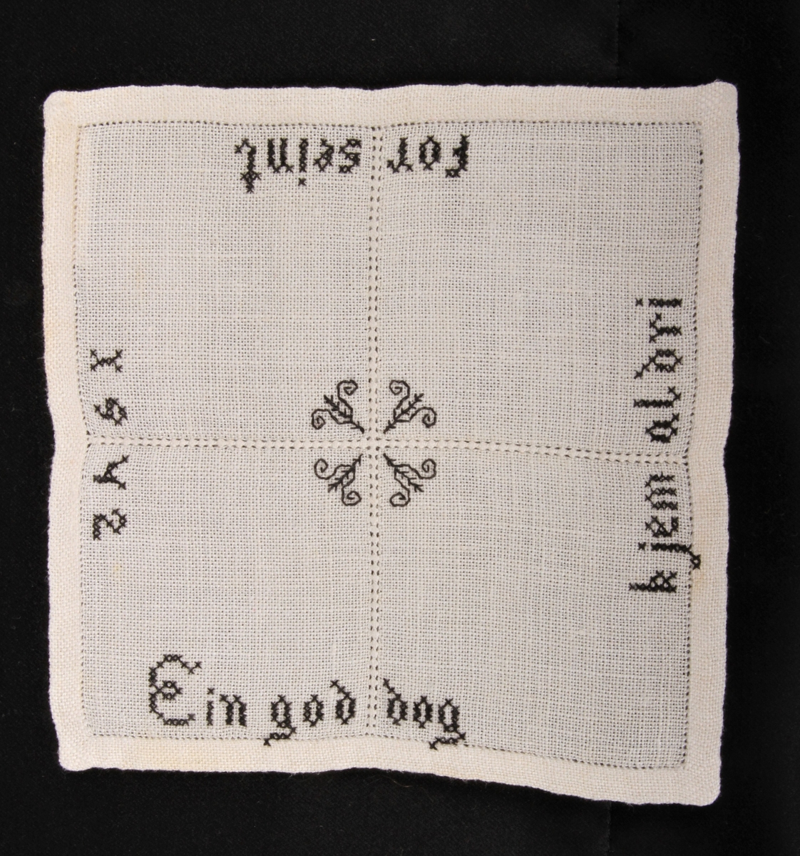 Natur bunn med svart dekor, brodert korsting, hullsøm og attersting. Border, tekst og blomster.