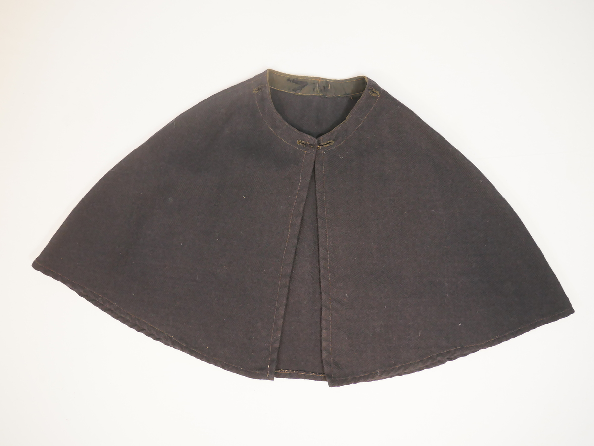 Enkel kappe av eitt bakstykke og to framstykke. Dobbelsaumar over skudrane/armane, alle saumar synlege som stikningar. Kanta på innsida av halsen med breitt bomullsband. Rundt halsringingen er det fem knapphol , kan dei ha vore til å feste ei hette?
Ingen opplysningar om bruk.