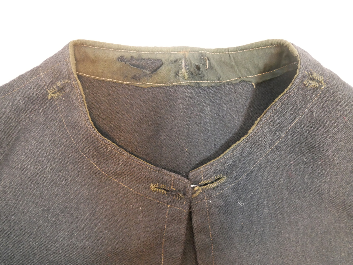 Enkel kappe av eitt bakstykke og to framstykke. Dobbelsaumar over skudrane/armane, alle saumar synlege som stikningar. Kanta på innsida av halsen med breitt bomullsband. Rundt halsringingen er det fem knapphol , kan dei ha vore til å feste ei hette?
Ingen opplysningar om bruk.