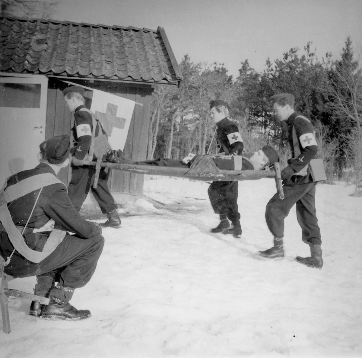 Soldater bär in en skadad man på räddningsbår till sjukkvarter vid sjukvårdsövning i fält vid F 11 Södermanlands flygflottilj, 1945. 

Vintertid.

Ur fotoalbum "Sjukvårdsskolan 15/1-15/3 1945" från F 11.