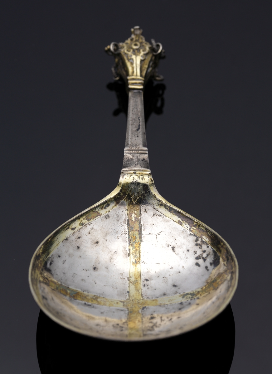 Brännvinssked av silver. 
S.k. kronsked med nästan runt skedblad, kort platt skaft, dekorerat med tvärräfflor längst ner. Skaftknopp i form av krona, 
sammansatt av fyra gotiska korsblommor. I kronans hörn hänger spiralvridna ringar (två saknas). 
Bladet har dekor i form av ett förgyllt kors med en graverad blomma i mitten. Även inre kanten av bladet är förgyllt. 
Stämplar och s.k. åldermansranka på skaftets baksida.

Inskrivet i huvudbok 1867.