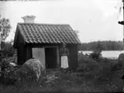 Byggnad, troligen tvättstuga, samt kvinna. Lillhärad socken, ca 1910.