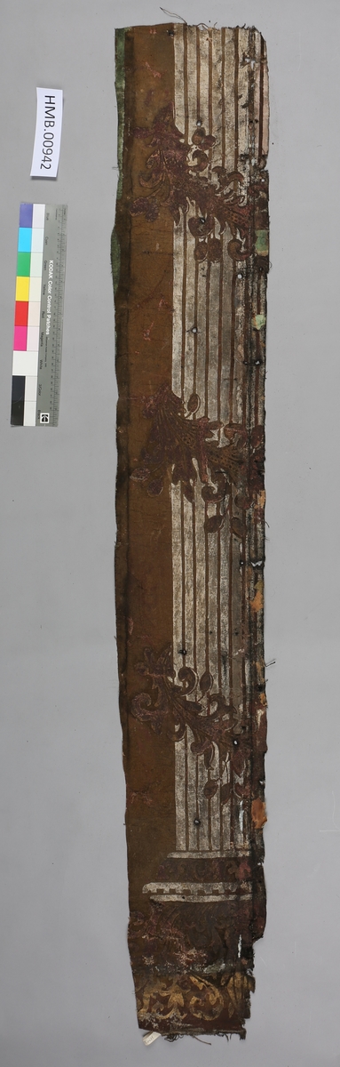 En hvit pilaster, tre ranker med planterornament (arkantus). Bakgrunnen er tilsynelatende beige, på siden er det en lysere grønnfarge. Helt øverst er det en forgylt ranke.