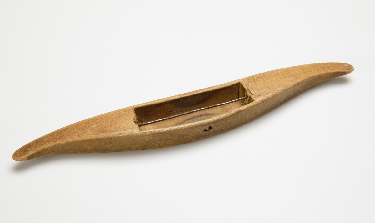Vävskyttel av trä (8 st).
Vågformad kontur. Avlångt hål med små benplattor omkring hålen för stången. 
a) med svart tråd
f) med tom tråd "tuta". 1894 skrivet med bläck.
Resterande skyttlar är tomma.

Mått:
Längd: 280 mm
Längd hål: 90-105 mm
Bredd: 35-45 mm