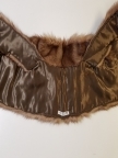 Midjelang stola, som kan lukkes med én kraftig hekte midt foran. Ved halsåpningen er skinnet splittet, slik at det fremkommer en effekt av et legg rundt nakken, med en ytre del som rager litt høyere enn det smalere stykket innerst mot halsen. Øvre del har søm midt bak, og skinnet er brettet inn mot nakken. På grunn av splitten som er skåret på hver side av nakken, dannes det et skrått skulderparti. Nedenfor skuldrene er det skjøtt på lange, jevnt brede og avrundede forstykker.  Plagget er fôret, og har en stor fuktskjold på den ene siden. Fôret er av blank, myk, silkeaktig sateng, men kan kanskje være sekundært og av syntetfiber. Ingen spor etter etikett. Pelsverket er fra dyrets ryggstykke, og er anvendt slik at den mørke stripen fra ryggstykket danner et dekorativt element.