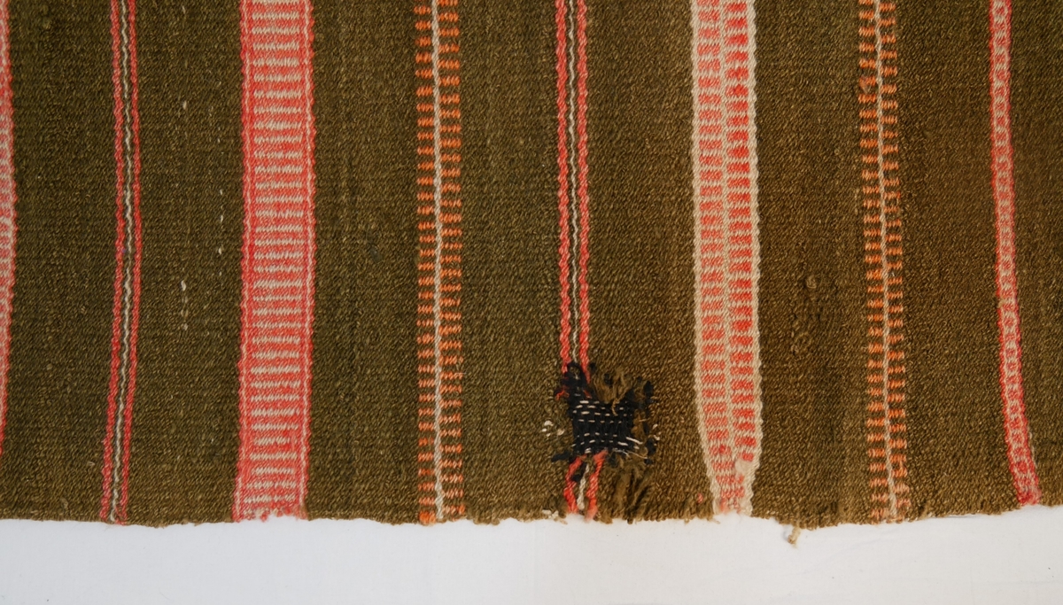 Åklet er samansytt av to lengder og falda i begge endane. Det er bøtt med mørk farge to stader.