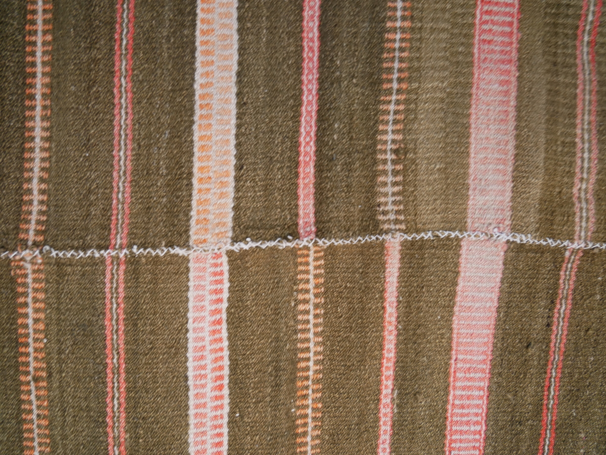 Åklet er samansytt av to lengder og falda i begge endane. Det er bøtt med mørk farge to stader.