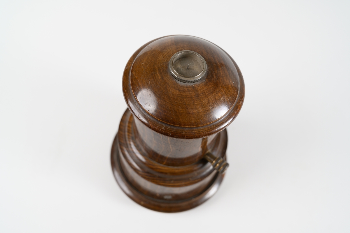 Avmagnetiseringsapparat för borttagande av magnetism i klocka. Apparaten består av en rund, svarvad behållare med lock. Under locket finns en bricka av metallnät, där objekt som ska avmagnetiseras placeras. Avmagnetiseringsmekaniken under bricka är av mässing. På sidan av träbehållaren sitter en mässingsskruv som har kontakt med insidans utrustning. Lodrät spricka i träbehållaren.