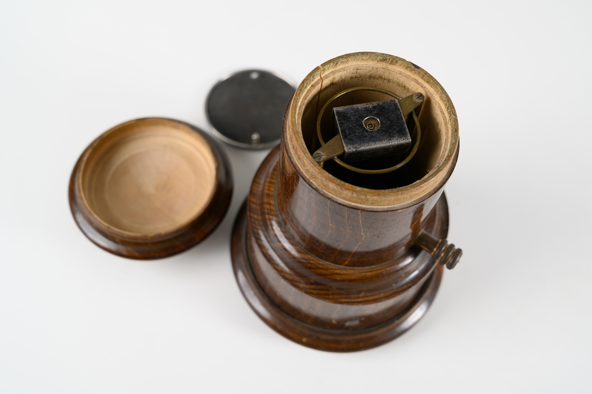 Avmagnetiseringsapparat för borttagande av magnetism i klocka. Apparaten består av en rund, svarvad behållare med lock. Under locket finns en bricka av metallnät, där objekt som ska avmagnetiseras placeras. Avmagnetiseringsmekaniken under bricka är av mässing. På sidan av träbehållaren sitter en mässingsskruv som har kontakt med insidans utrustning. Lodrät spricka i träbehållaren.