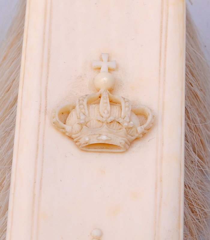 Gräddfärgad borste med handtag av elfenben och borst av animaliskt material, troligtvis gethår. Handtaget är format efter dess ornament som liknar akantusblad, mitt på handtaget finns pärlstavsdekor. Handtagets ornamentering fortsätter i relief en bit upp på borstens rygg. Ryggen är rektangulär och på mitten finns en kungakrona i relief.