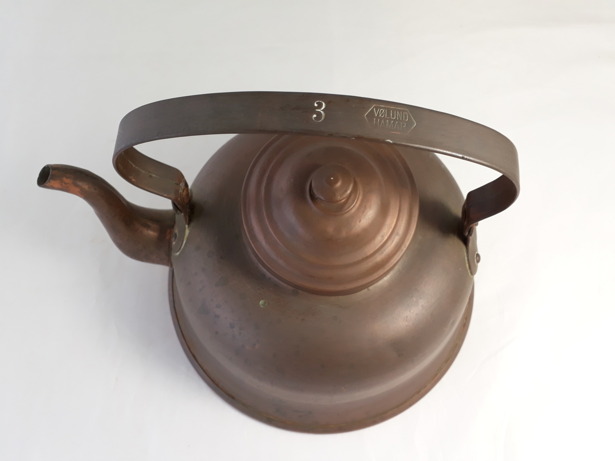 Kaffekjele i kobber med lokk. Sirkulær med innsnevring mot lokket og utvidelse mot en bredere fotkant. Hankfestet ved tuten og på motsatt side.