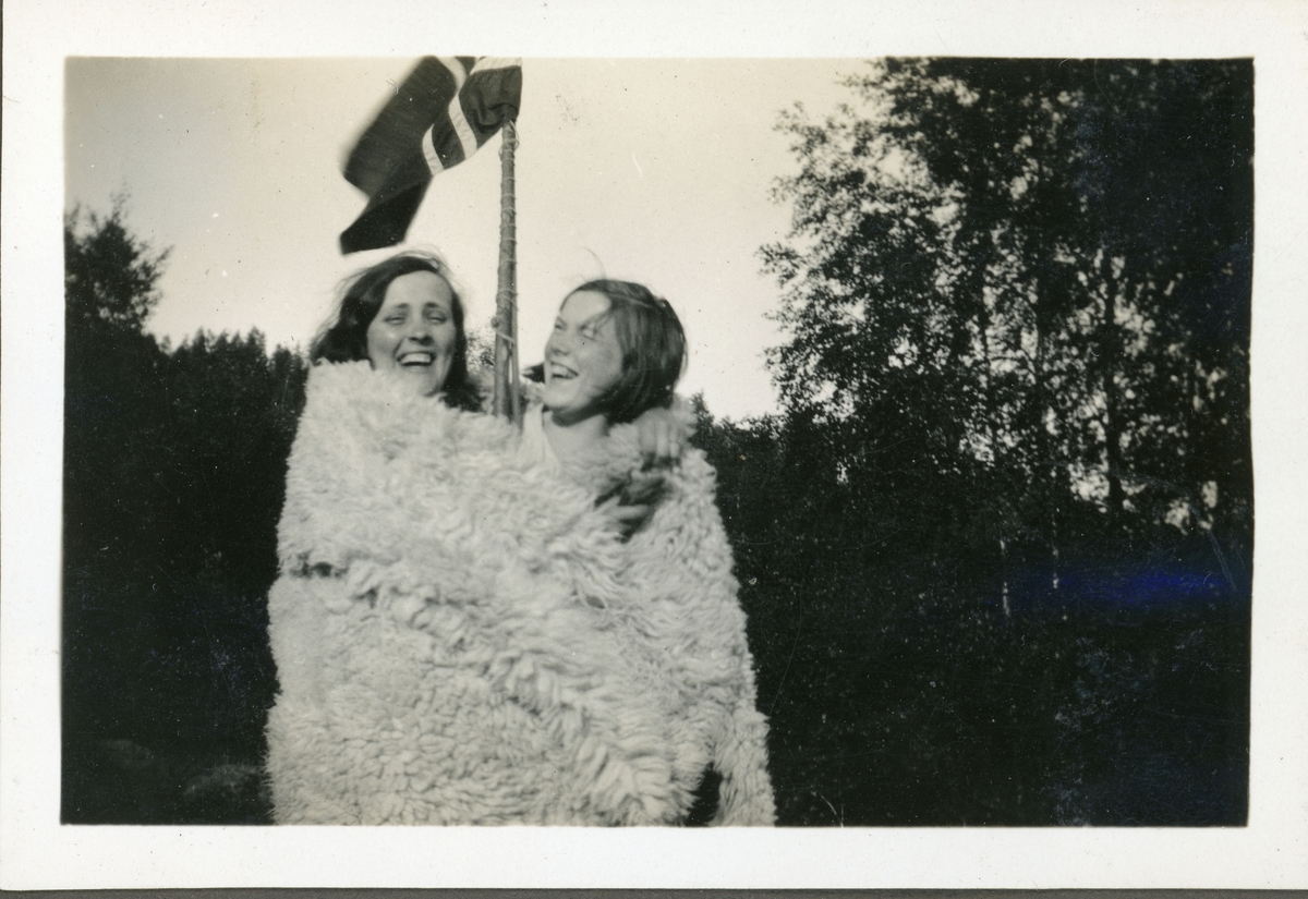 To jenter i skinnfell foran flaggstang. Ingelsrudsjøen. Trolig 1930-tall.