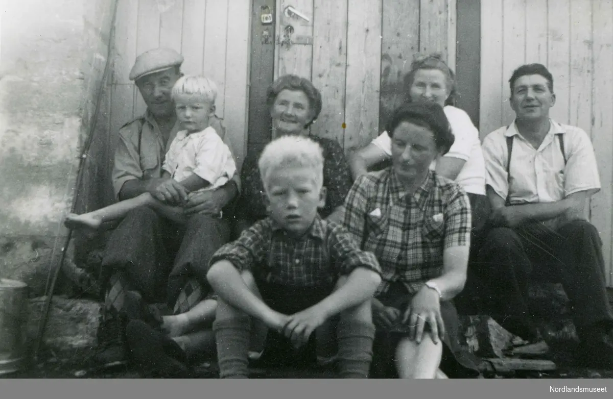 Gruppe mennesker fotografert ved en hytte ved Nordfoldvatnet i aug. 1953.
Fra venstre Jon Olsen med Rolf Willumsen på fanget, Hilma Olsen, ukjent, Henry Bergvoll.
Foran Knut Willumsen og Inger Normann.