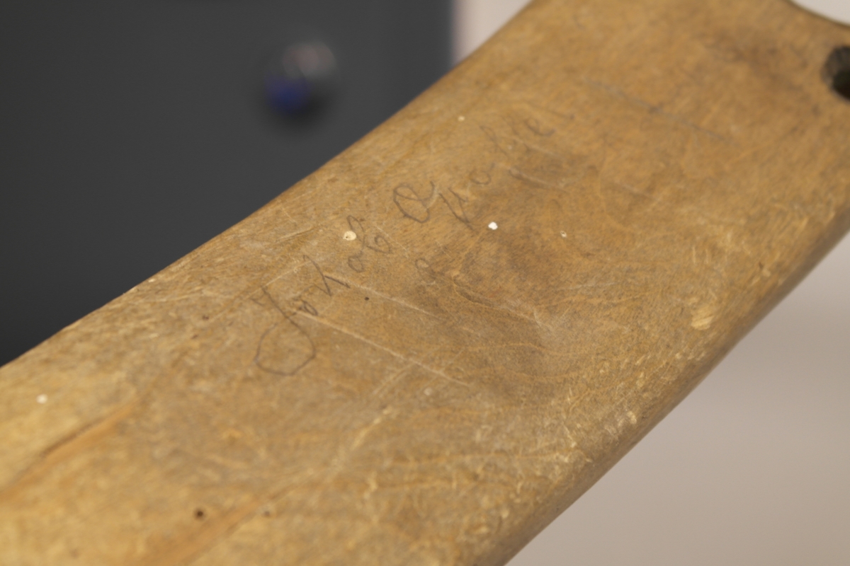 Sauestokk i tre. Stokken er buet og har en rund utsparing på midten samt to små hull på hver side av utsparingen. På den ene siden er det inngravert ett kryss samt et håndskrevet personnavn. En merkelapp med håndskrevet tekst har vært festet til stokken med hyssing. Stokken ble brukt for å hindre sau å hoppe over gjerde o.l. ved å feste den til sauens ben.