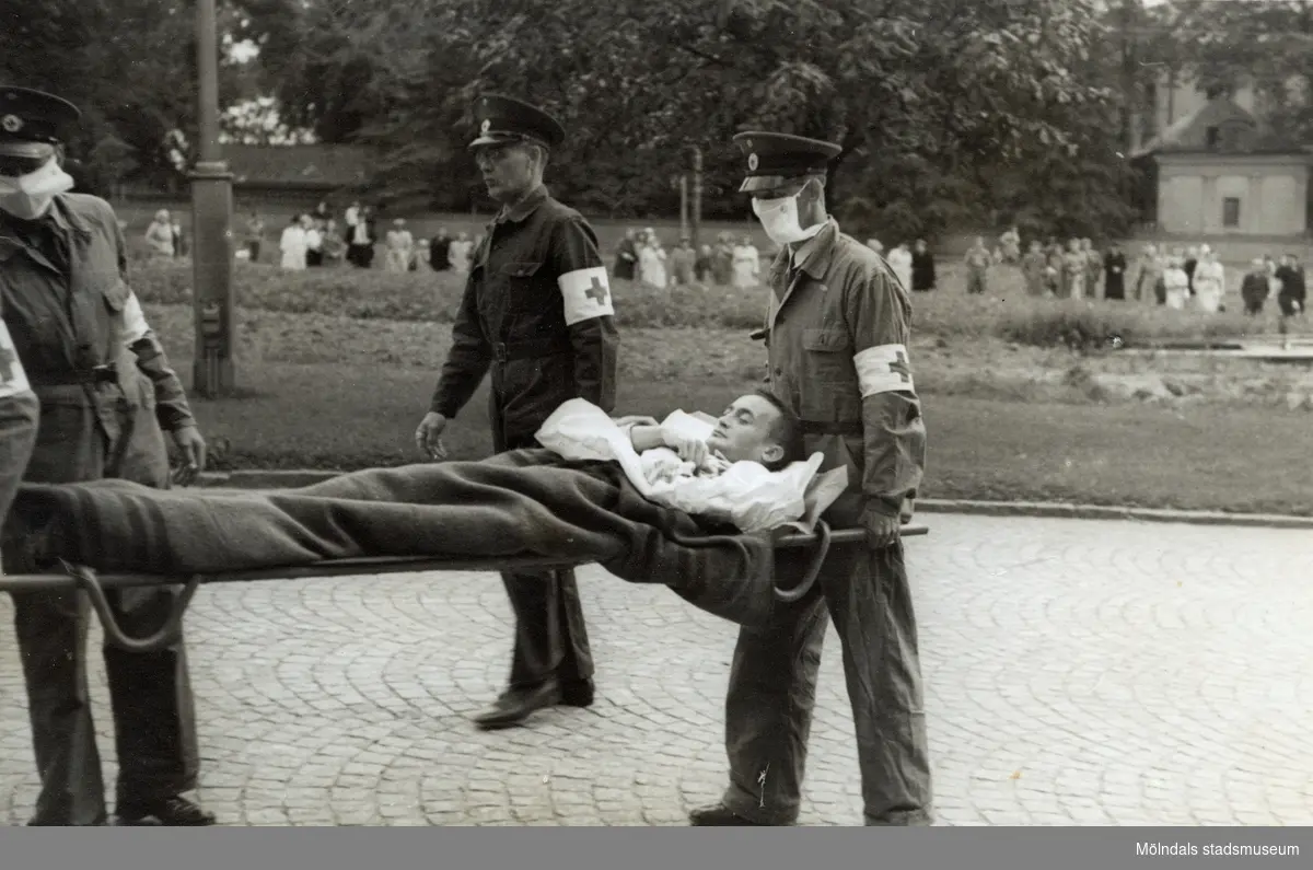 "Karantänsförläggning" på Kvarnbyskolan för överlevande från koncentrationsläger i Tyskland och Polen 1945.  
Skolan fungerade under denna sommar som beredsskapssjukhus.

En manlig flykting blir buren på bår av Röda Korsets personal.