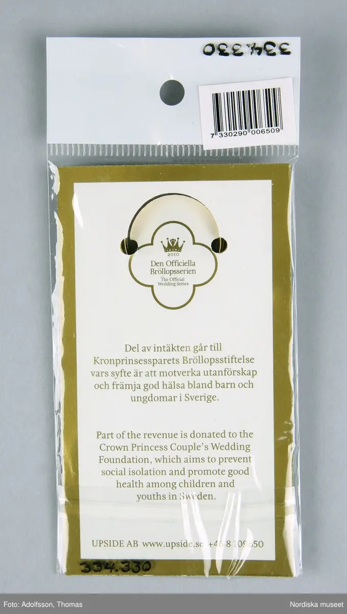 Nyckelring, i originalförpackning av transparent plast och papper. Nyckelringen består av en öppningsbar ring, en medalj med Den Officiella Bröllopsseriens logotyp av metall. Ringen och medaljen är sammanfogade med en rem av konstläder som hålls samman av en metallklipps. Ringen är fäst i en pappersbakgrund i förpackningen. På förpackningen en etikett med streckkod och artikelnummer. Ingår i "Den officiella Bröllopsserien". Se ref.materal ”Den Officiella Bröllopsserien” och www.upside.se

På nyckelringen: "2010", på förpackningen: "20102010 Den Officiella bröllopsserien The official Wedding Series Del av intäkterna går till Kronprinsessparets  Bröllopsstiftelse vars syfte är att motverka utanförskap och främja god hälsa bland barn och ungdomar i Sverige.","Part of the revenue is donated to the Crown Prinsess Couple's Wedding Foundation, which aims to prevent social isolation and promote good health among children and youths in Sweden", " UPSIDE AB www.upside.se +468109650