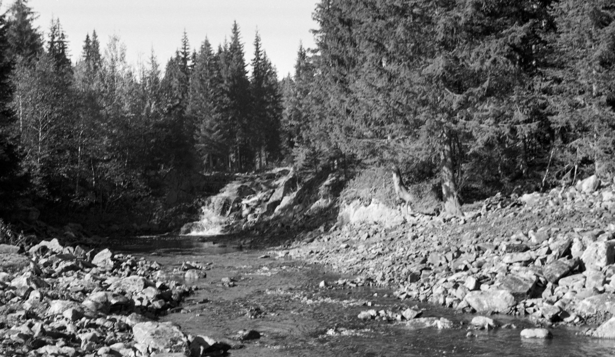 Elveløpet i Løsetåa i Nord-Odal, fotografert under Brattfossen, like ovenfor det stedet der Løsetåa forenes med Mørkåa og blir til Kilåa, som etter 4-500 meter renner ut på vestsida av innsjøen Råsån. I forgrunnen kan det se ut til at man har ryddet midtålen i elva for stein med sikte på å skape en passasje der det var overkommelig å få fram fløtingstømmeret. Arbeidet er sannsynligvis utført med bulldoser. Dette fotografiet ble tatt sommeren 1954, i en periode med svært lav vannføring.