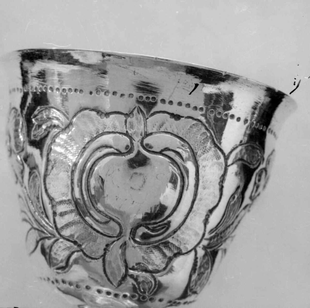 Beger av sølv. Begeret har stett og rund sokkel. På klokken er det to border med dekorative punslinger, mellom bordene er det drevet dekor av blomster. Siselert bølgedeker på sokkel.