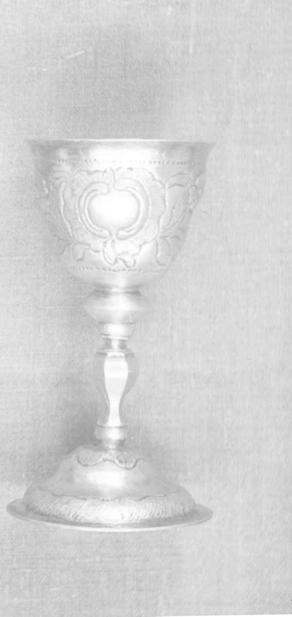 Beger av sølv. Begeret har stett og rund sokkel. På klokken er det to border med dekorative punslinger, mellom bordene er det drevet dekor av blomster. Siselert bølgedeker på sokkel.