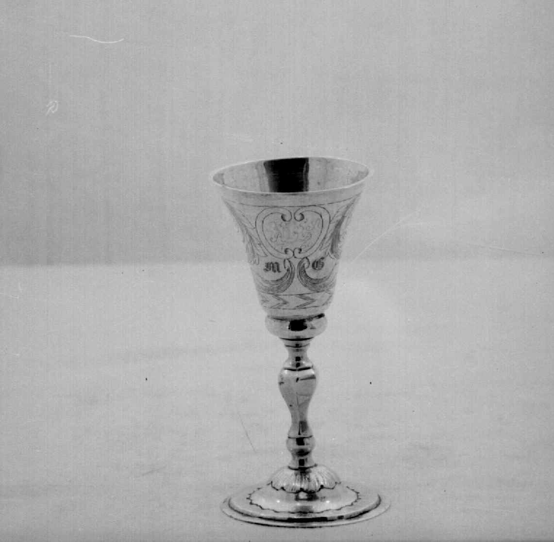 Beger av sølv. Begeret har stett og rund sokkel. På klokken er det to border med dekorative punslinger, mellom bordene er det drevet dekor av blomster. Siselert bølgedeker på sokkel.