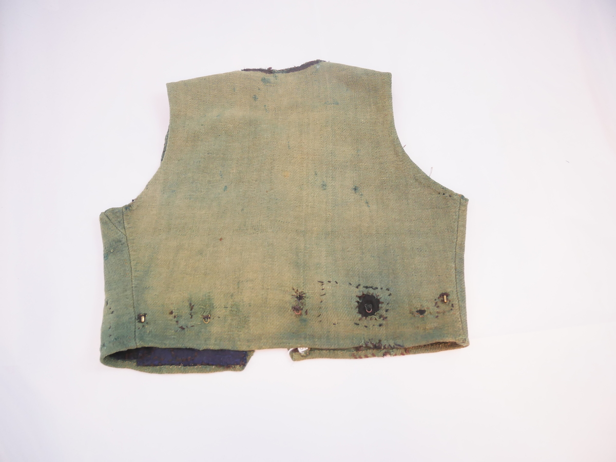 Livstykke som er overdel til kvinnedrakt. Livstykke i grønn ull med firskoren halsopning. Skal festast heilt ihop framme med 11 sett hekter og hemper. Hekter og hemper rundt livet til feste for skjørt. Rundt ermeopningane har det vore enkel fald, seinare er dette stadvis forsterka med overkast av grov tråd. Det same er tilfellet rundt halsopningen der det opphavleg har vore svart ullband. Livstykket er reparert med svarte og blå bøter i nedkant. Framkanten på livet er runda for å lage plass til bysten.