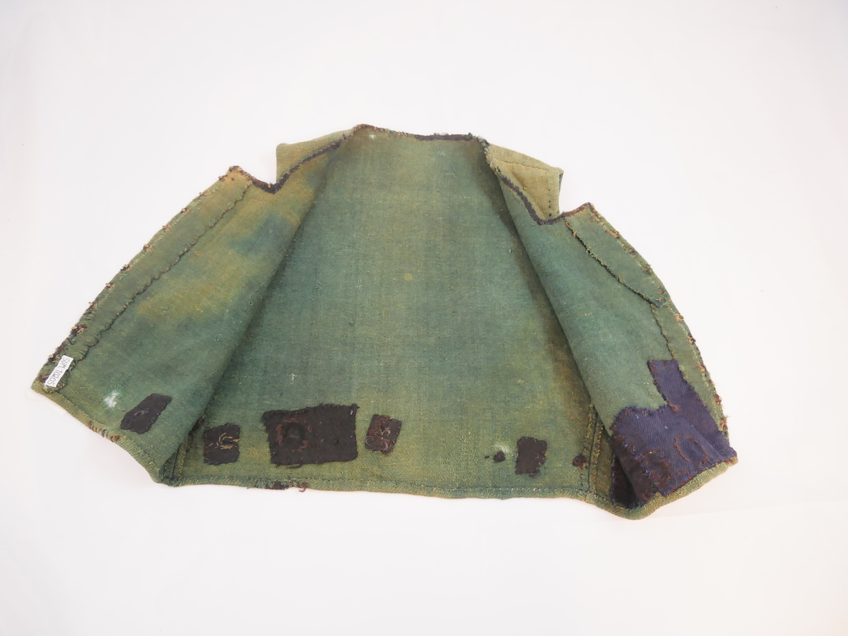 Livstykke som er overdel til kvinnedrakt. Livstykke i grønn ull med firskoren halsopning. Skal festast heilt ihop framme med 11 sett hekter og hemper. Hekter og hemper rundt livet til feste for skjørt. Rundt ermeopningane har det vore enkel fald, seinare er dette stadvis forsterka med overkast av grov tråd. Det same er tilfellet rundt halsopningen der det opphavleg har vore svart ullband. Livstykket er reparert med svarte og blå bøter i nedkant. Framkanten på livet er runda for å lage plass til bysten.