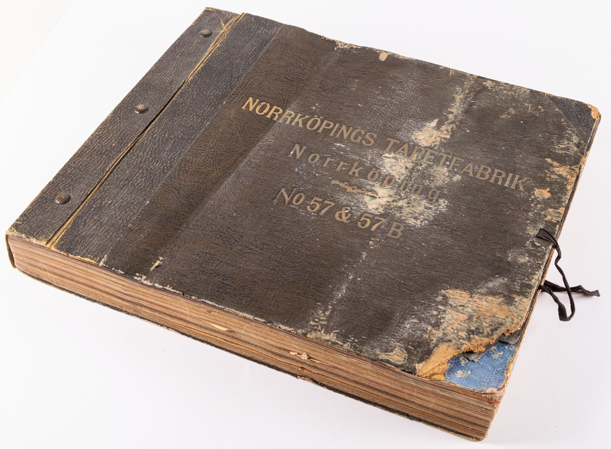 Tryckt tapetkatalog från Norrköpings tapetfabrik. Bruna hårda pärmar, brun rygg. Text i på pärmens framsida: "Norrköpings tapetfabrik No. 57 & 57B". innehåller prov på arsenikfria tapeter och bårder.