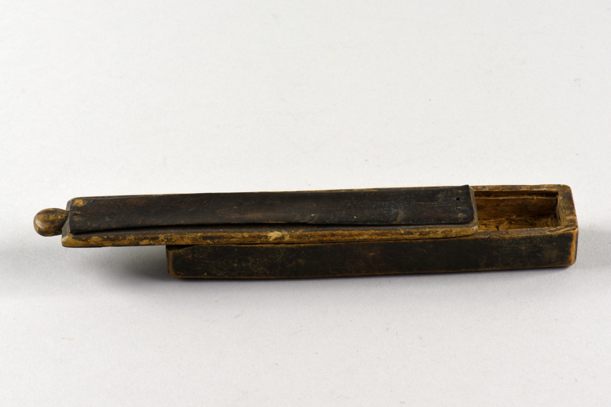 Rektangulärt fodral för rakdon med skjutlock. Tillverkat av björk, locket är klätt med läder för att användas vid strigling. På undersidan inristningar bland annat med årtalet 1726.
