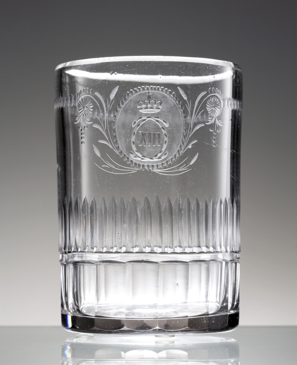 Dricksglas. Tillhör "Carl XIII:s servis".
Blåst 1810-1813. Graverat 1815-1818.
Graverat av Anders Spolander. Se E. Steenberg "Svenskt adertonhundratals glas", sidan 131,1).
Beskrivning: Cylindriskt. Monogram "C XIII" med krona, i en oval omgiven av stiliserade växter. Bård av små oliver och streck. Rad av ställda skär i mittpartiet. Facettslipad nederdel.
Färg: Ofärgat klarglas.
Teknik: Slipad kant. Planslipad botten med kula. Slipad och graverad dekor enligt ovan.
Märkning: Graverat nr. under foten. Se "Signering, märkning" ovan.
Inskrivet i huvudkatalogen tidigast 1976.

Enligt uppgift ägdes en del av servisen av Växjö regemente tills regementet upplöstes år 18??. Skänktes sedan till regementets officerare. Dessa pjäser tillhörde fänrik ....

Gravör Anders Spolander, född i Umeå den 27 juli 1782, arbetade som glassliparlärling vid Strömbäcks glasbruk 1806-1812, vid Kungsholms glasbruk 1812-1813, och 1813 vid en egen verkstad för "glasritning". Dog 1836. Hans verkstad drevs av änkan till 1843.
Funktion: Dricksglas