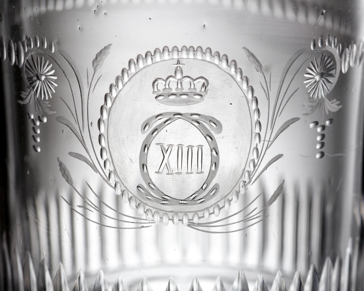 Dricksglas. Tillhör "Carl XIII:s servis".
Blåst 1810-1813. Graverat 1815-1818.
Graverat av Anders Spolander. Se E. Steenberg "Svenskt adertonhundratals glas", sidan 131,1).
Beskrivning: Cylindriskt. Monogram "C XIII" med krona, i en oval omgiven av stiliserade växter. Bård av små oliver och streck. Rad av ställda skär i mittpartiet. Facettslipad nederdel.
Färg: Ofärgat klarglas.
Teknik: Slipad kant. Planslipad botten med kula. Slipad och graverad dekor enligt ovan.
Märkning: Graverat nr. under foten. Se "Signering, märkning" ovan.
Inskrivet i huvudkatalogen tidigast 1976.

Enligt uppgift ägdes en del av servisen av Växjö regemente tills regementet upplöstes år 18??. Skänktes sedan till regementets officerare. Dessa pjäser tillhörde fänrik ....

Gravör Anders Spolander, född i Umeå den 27 juli 1782, arbetade som glassliparlärling vid Strömbäcks glasbruk 1806-1812, vid Kungsholms glasbruk 1812-1813, och 1813 vid en egen verkstad för "glasritning". Dog 1836. Hans verkstad drevs av änkan till 1843.
Funktion: Dricksglas