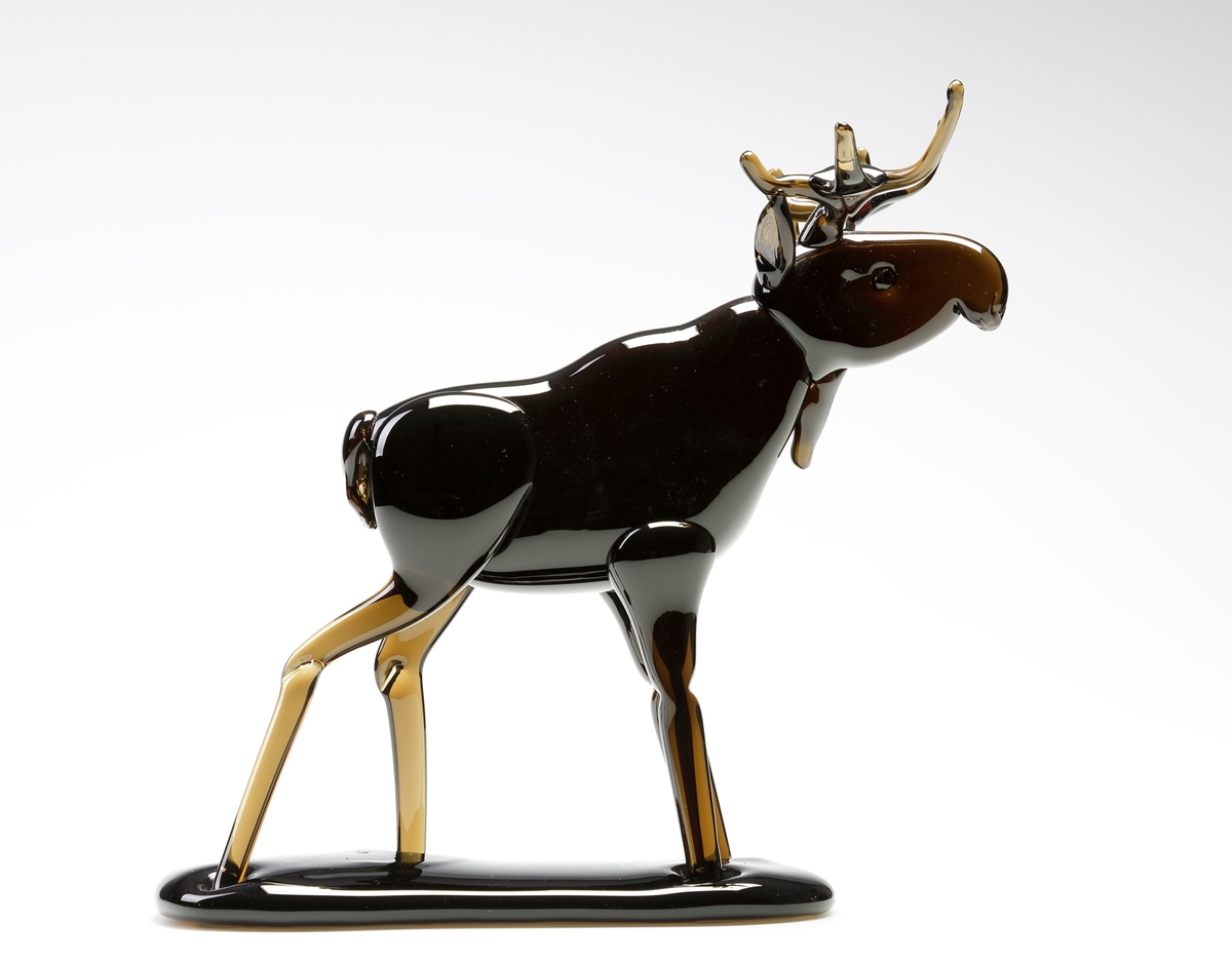 Skulptur. Formgiven av Nils Nilsson. Tillverkad av Joachim Nilsson. 
Följande text finns på ett reklamblad fasthäftat på registerkortet: "I slutet av 1940-talet började mästaren Nils Nilsson på sin fritid att tillverka glasälgar, som presenter till sina jaktkamrater. Älgen blev populär och efterfrågan ökade och Nils tog svärfar Harald (mästare på Berghems Glasbruk) till hjälp och på lördagseftermiddagarna efter arbetets slut träffades de i Berghem för att tillverka älgar. 
Älgen blev sedan ett signum för Nils och följde med honom från bruk till bruk. (Åseda, Eneryda, Hyllinge, Älghult m. fl.) När sonsonen Joachim 1985 började på glasbruk var farfar Nils redan pensionär, något som inte hindrade honom från att varje dag besöka bruket och ibland tillverka en älg. Joachim följde med stort intresse farfars skickliga arbete och snart prövade han sin första älg. Inget mästerverk precis - men den finns bevarad!!.
 I april 1995 startade Joachim tillsammans med bröderna Jesper och Jacob produktionen på anrika Gullaskrufs Glasbruk, som då legat nere en tid. Idag tilllverkar Joachim med hjälp av Jesper glasälgar med en elegans och hantverksskicklighet som farfar Nils skulle ha varit stolt över. Familjetraditionen lever vidare. Glasälgarna från Gullaskruf är signerade och numrerade".
Beskrivning: Älgtjur, friblåst med påklipp.
Färg: Brun.
Inskrivet i huvudkatalogen tidigast 1996.
Funktion: Prydnadfigur i form av en älgtjur.