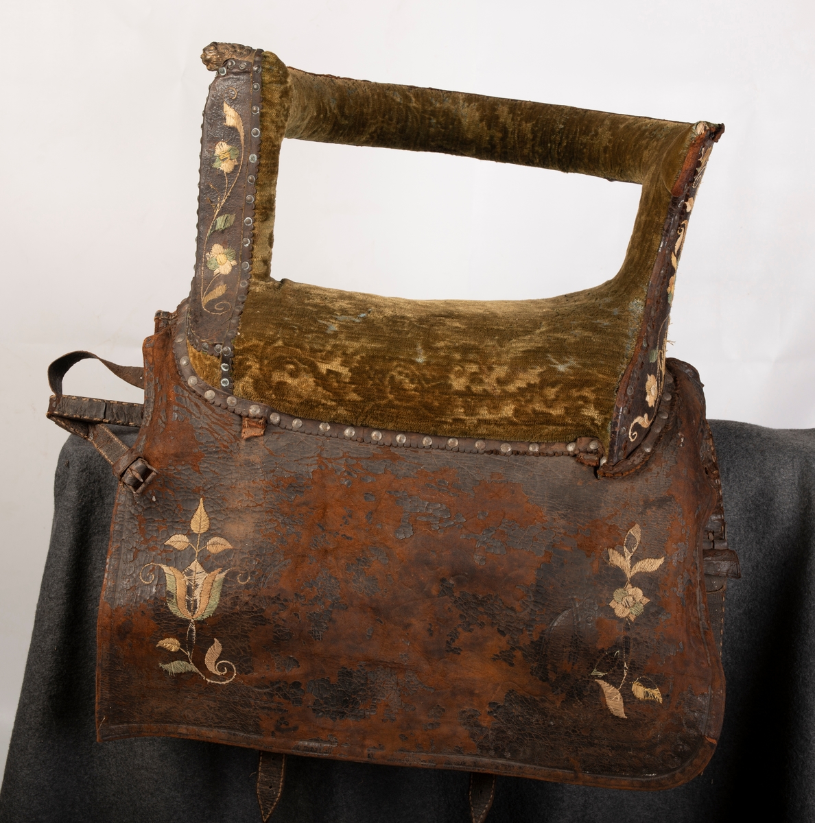Brodert lær. Grønn mønstret  fløyel i setet og på armlene. Messinghode på fremre del av rygglenet. Initialene KDS og årstallet1773 brodert på. Løs narv på kappene, redrot.
