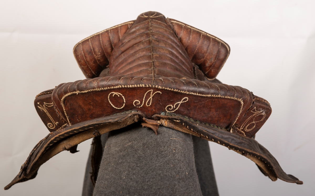 Lærtrukket sadel fra 1778. Initialene ONS brodert. Kapper med preget lær. 