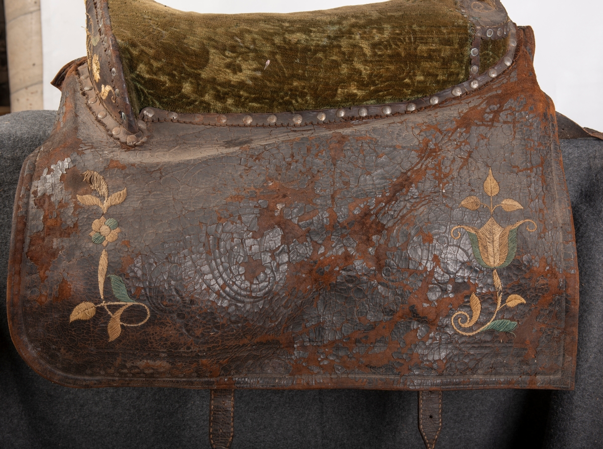 Brodert lær. Grønn mønstret  fløyel i setet og på armlene. Messinghode på fremre del av rygglenet. Initialene KDS og årstallet1773 brodert på. Løs narv på kappene, redrot.