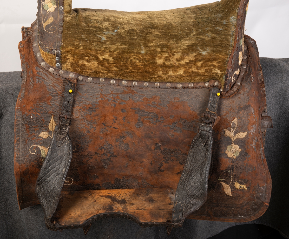 Brodert lær. Grønn mønstret  fløyel i setet og på armlene. Messinghode på fremre del av rygglenet. Initialene KDS og årstallet1773 brodert på. Løs narv på kappene, redrot.